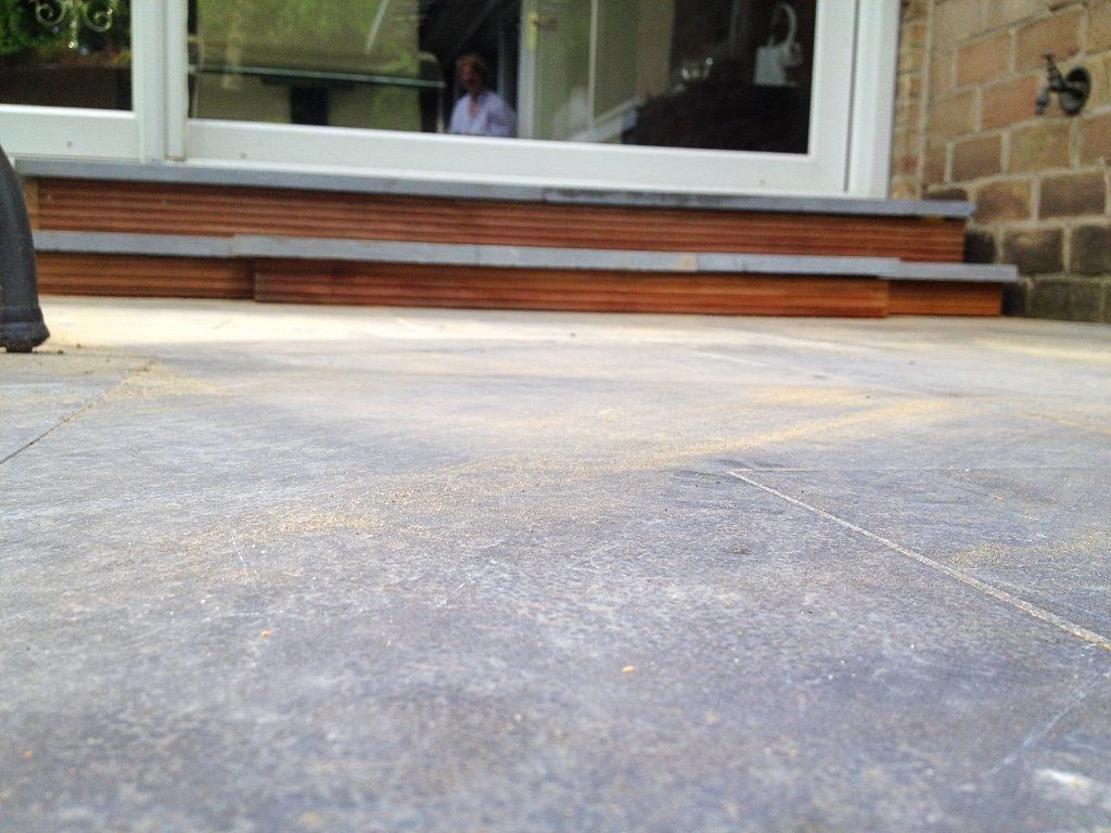 Laag perspectief van een donkergrijs stenen terras dat leidt naar houten trappen voor een glazen deur.