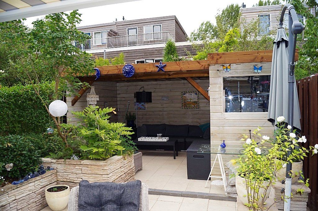 Terras in de achtertuin met houten constructie, zitgelegenheid en planten.