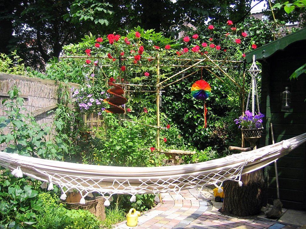 Achtertuin: hangmat, waslijn met rode rozen, hangende plantenbakken, kleurrijke decoratie.