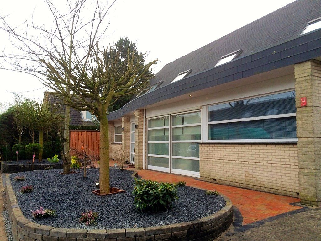 Een huis met een bloembed van zwarte natuursteen en een pad van bakstenen.