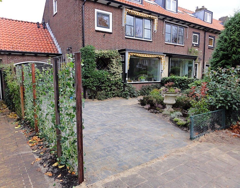 Bakstenen huis met oranje pannendak, grindoprit en schutting van klimplanten.