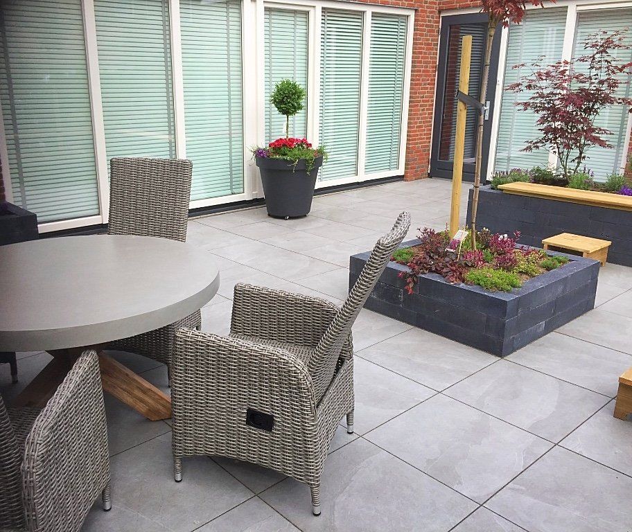 Terras met een ronde tafel en stoelen, bloempotten en een bakstenen gebouw op de achtergrond.