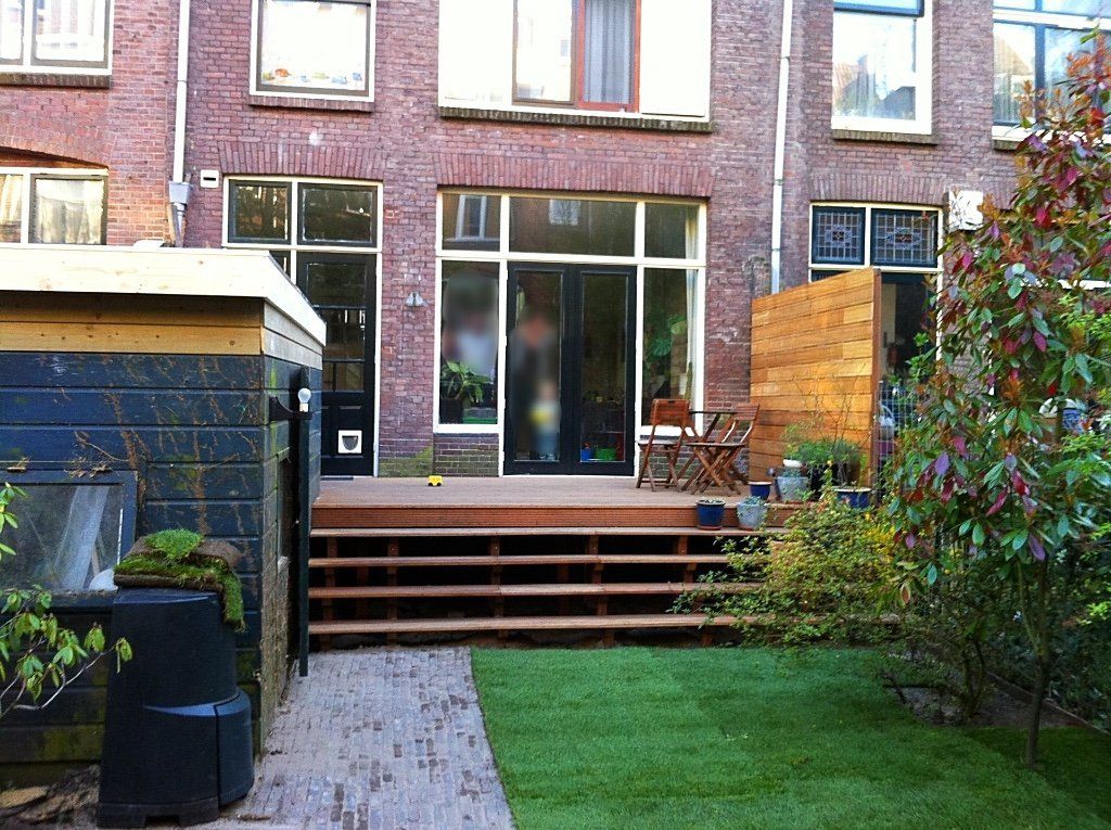Achtertuin met terras, gazon, stenen bijgebouw en houten schutting.
