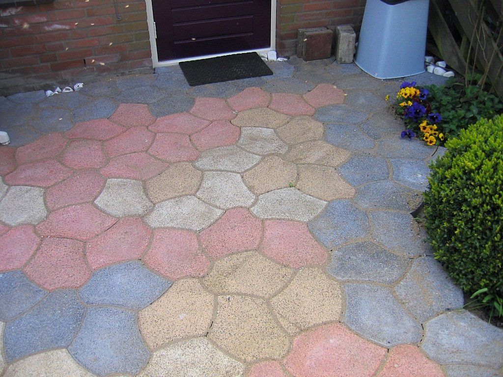Kleurrijke, onregelmatige bestrating vormt een terras voor een deur. Roze, beige, blauwe en grijze stenen vormen een mozaïekpatroon.