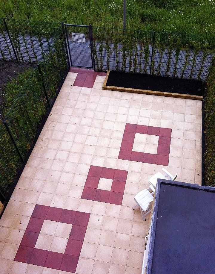 Terras met rode en beige vierkante tegels, een bloembed en een klein metalen hekje.