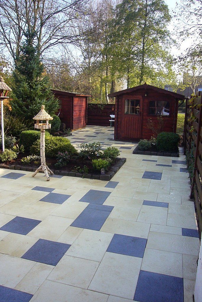 Terras met geblokte tegels, kleine bloembedden, houten schuurtjes en een vogelvoederhuisje.