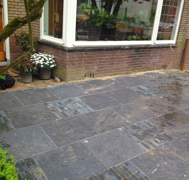 Een donkerstenen terras voor een bakstenen gebouw met grote ramen en potplanten.