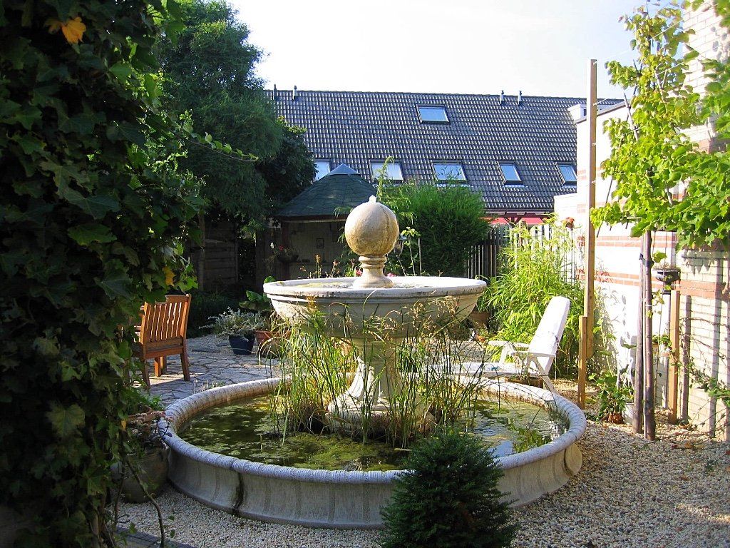 Stenen fontein in een binnentuin, omgeven door planten en een gebouw met dakramen.