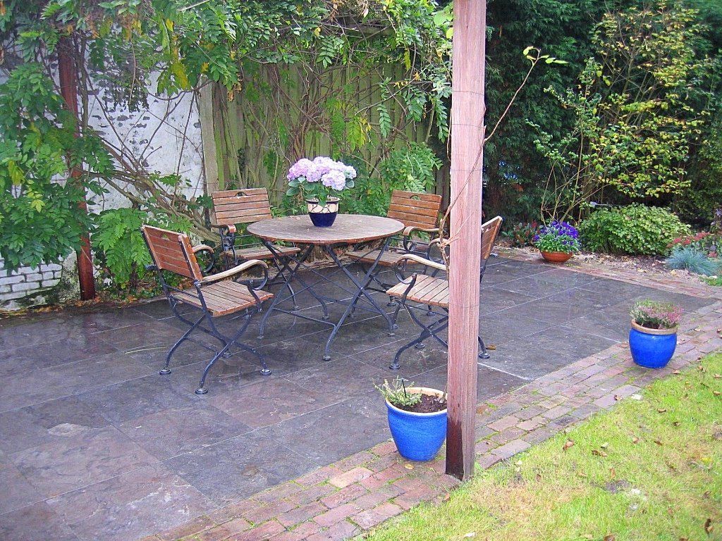 Terras met tafel en stoelen, omgeven door groen en potplanten.