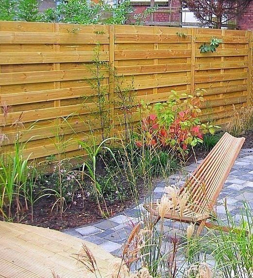 Houten schutting met een tuin ervoor en een gevlochten stoel.