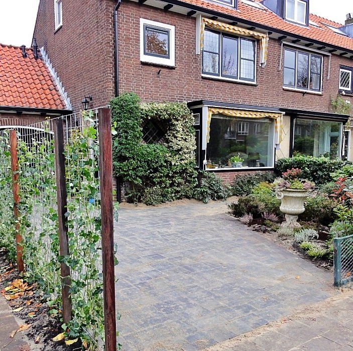 Bakstenen huis met een kleine tuin en oprit. Aan de linkerkant loopt een hek.