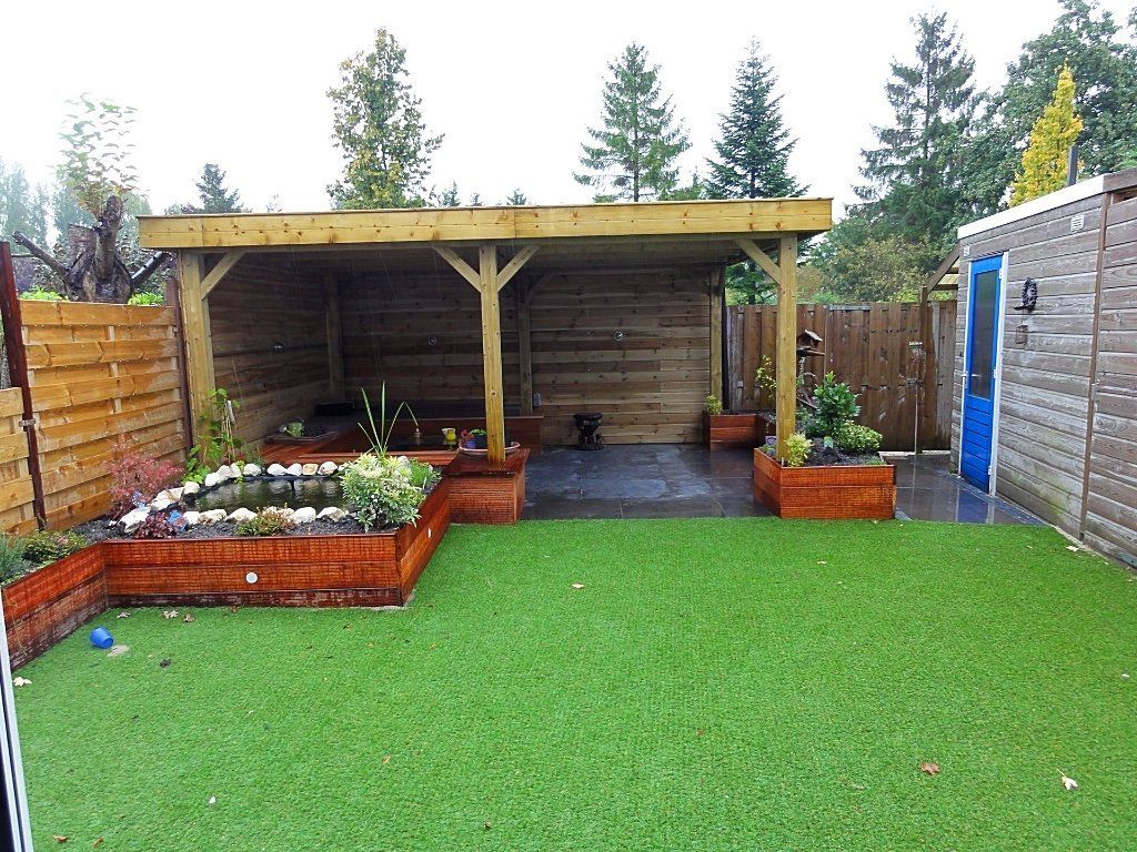 Achtertuin met een houten overkapping, een vijver en groen kunstgras.