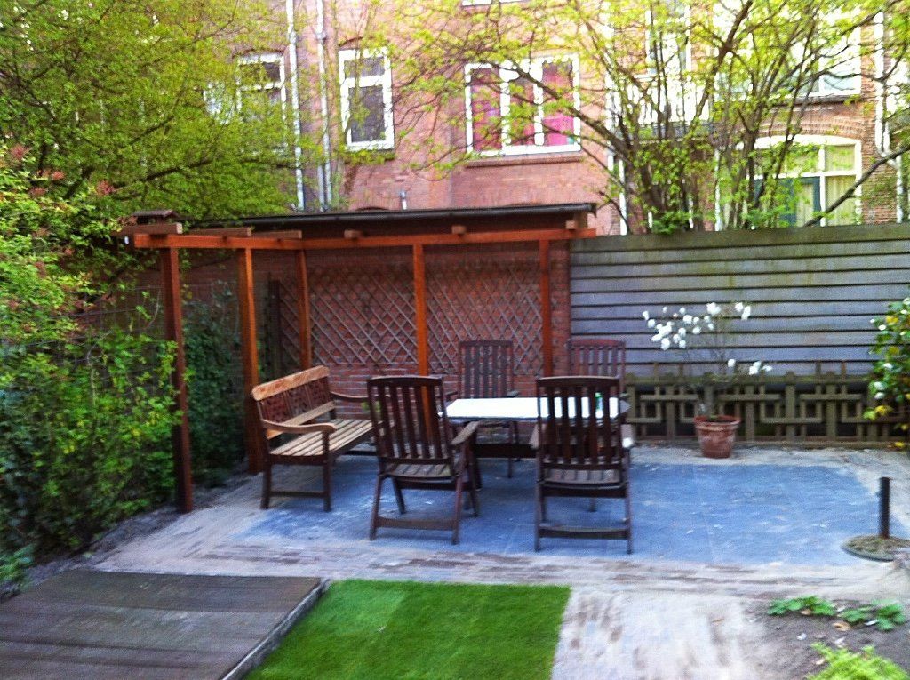 Terras met een tafel, stoelen, een bank en een pergola. Op de achtergrond is een bakstenen gebouw te zien.