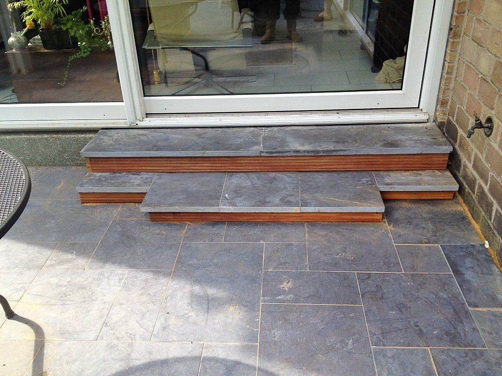 Terrastrap met drie treden, een bakstenen muur aan de rechterkant en een glazen schuifdeur.