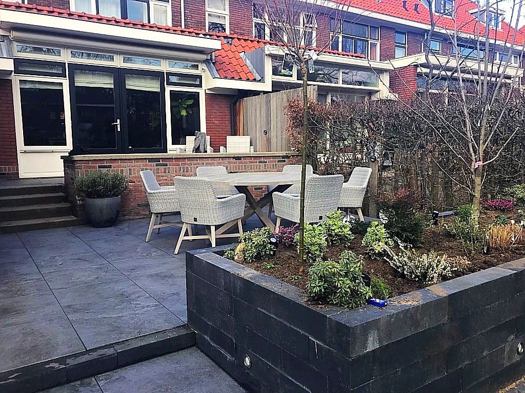 Buitenpatio met eethoek en verhoogd tuinbed, grenzend aan een bakstenen gebouw.