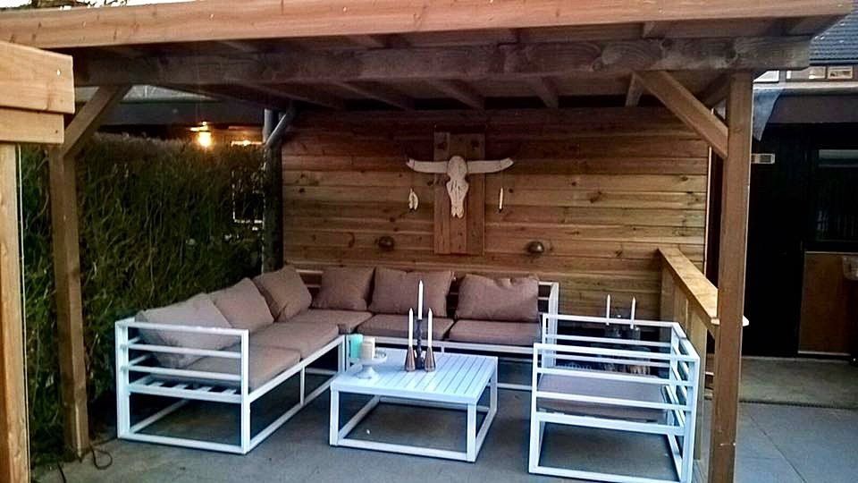 Buitenpatio met wit meubilair, houten pergola en decoratieve muur.