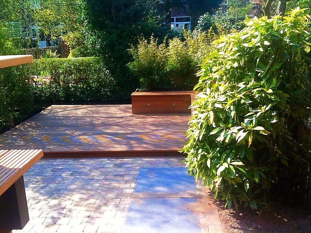 Houten terras met ingebouwde plantenbak, omgeven door groen en een bakstenen pad.