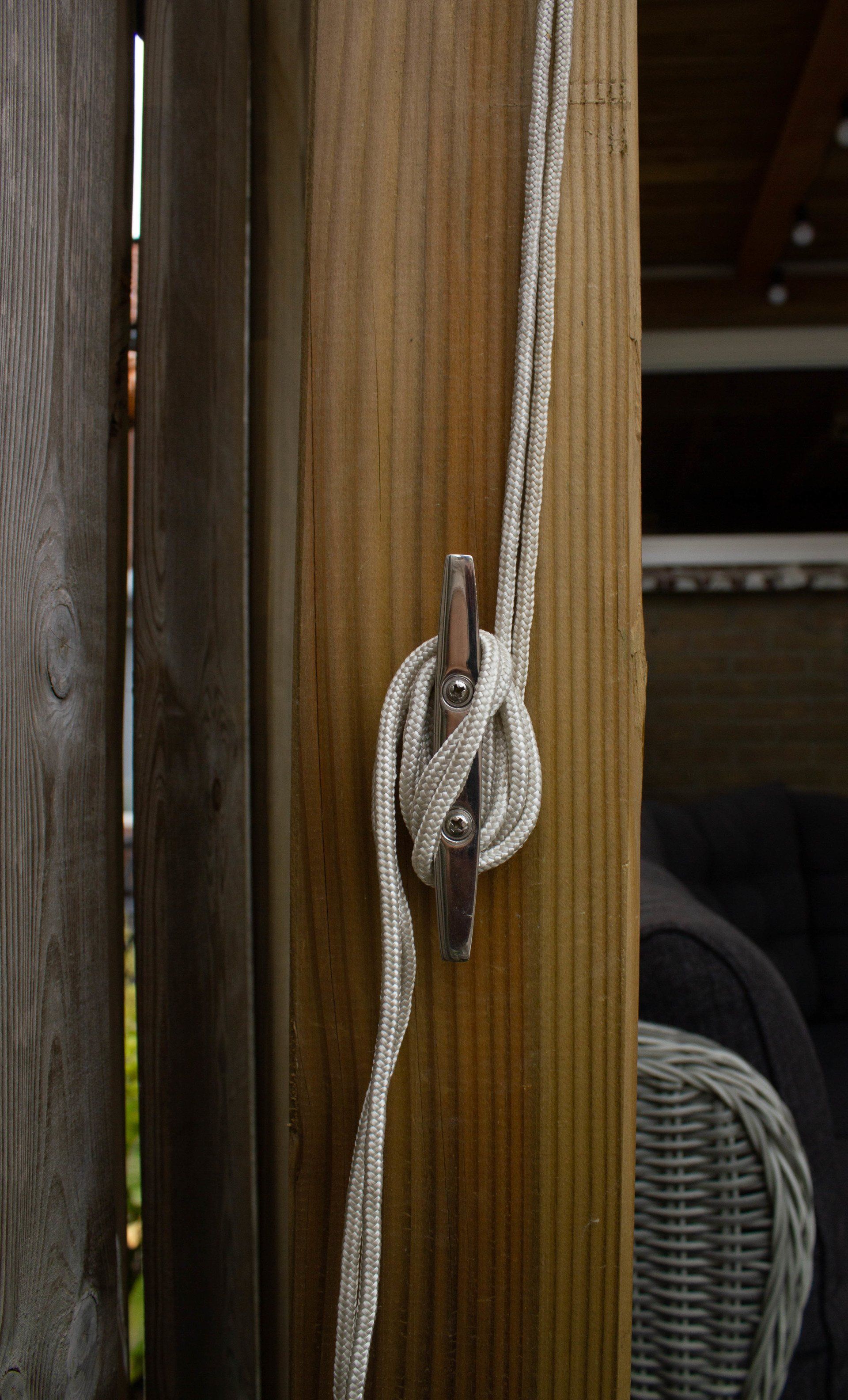 Wit touw vastgebonden aan een houten paal met een metalen klem.