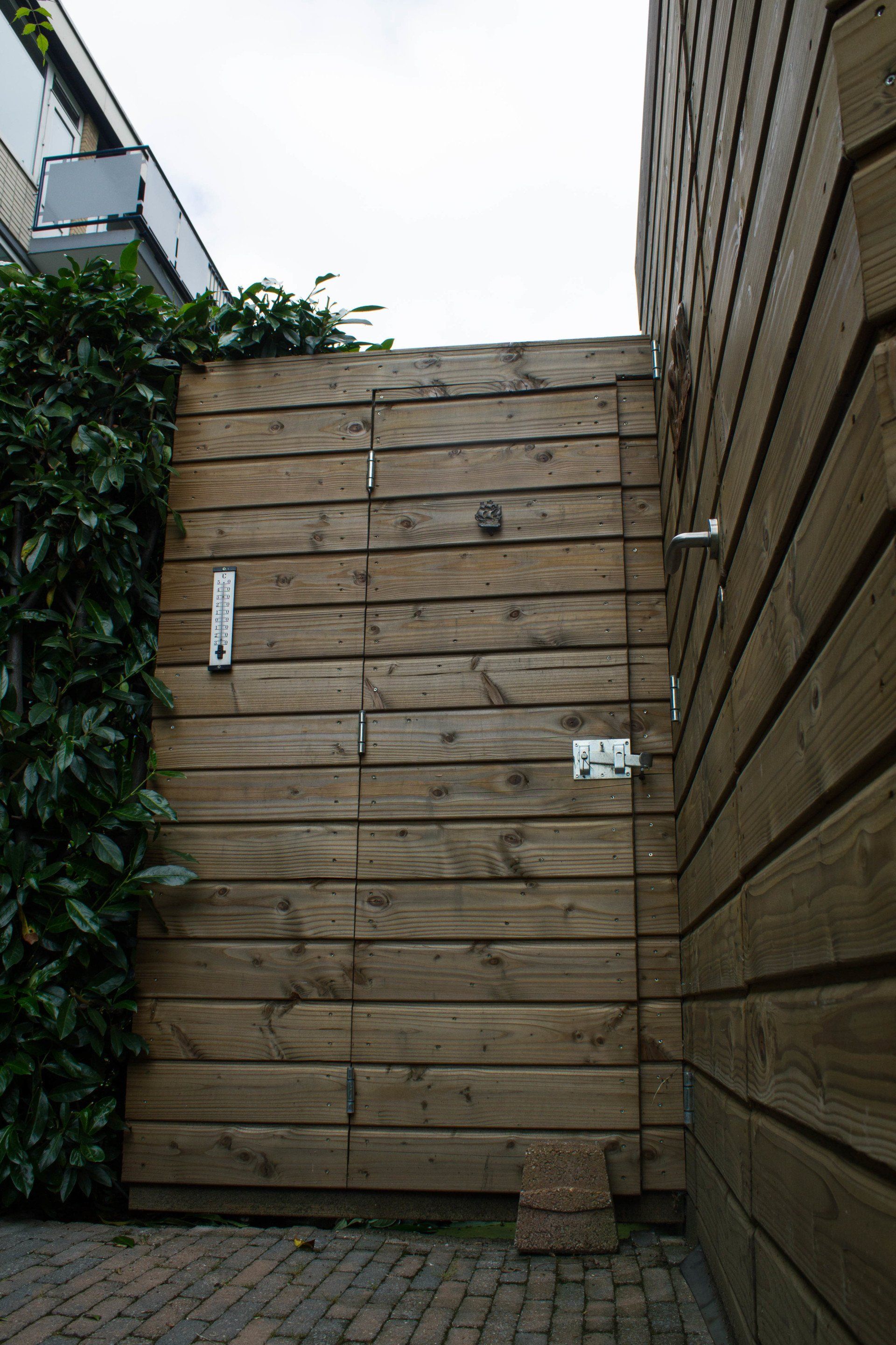 Houten poort en muur met groen gebladerte aan de linkerkant.