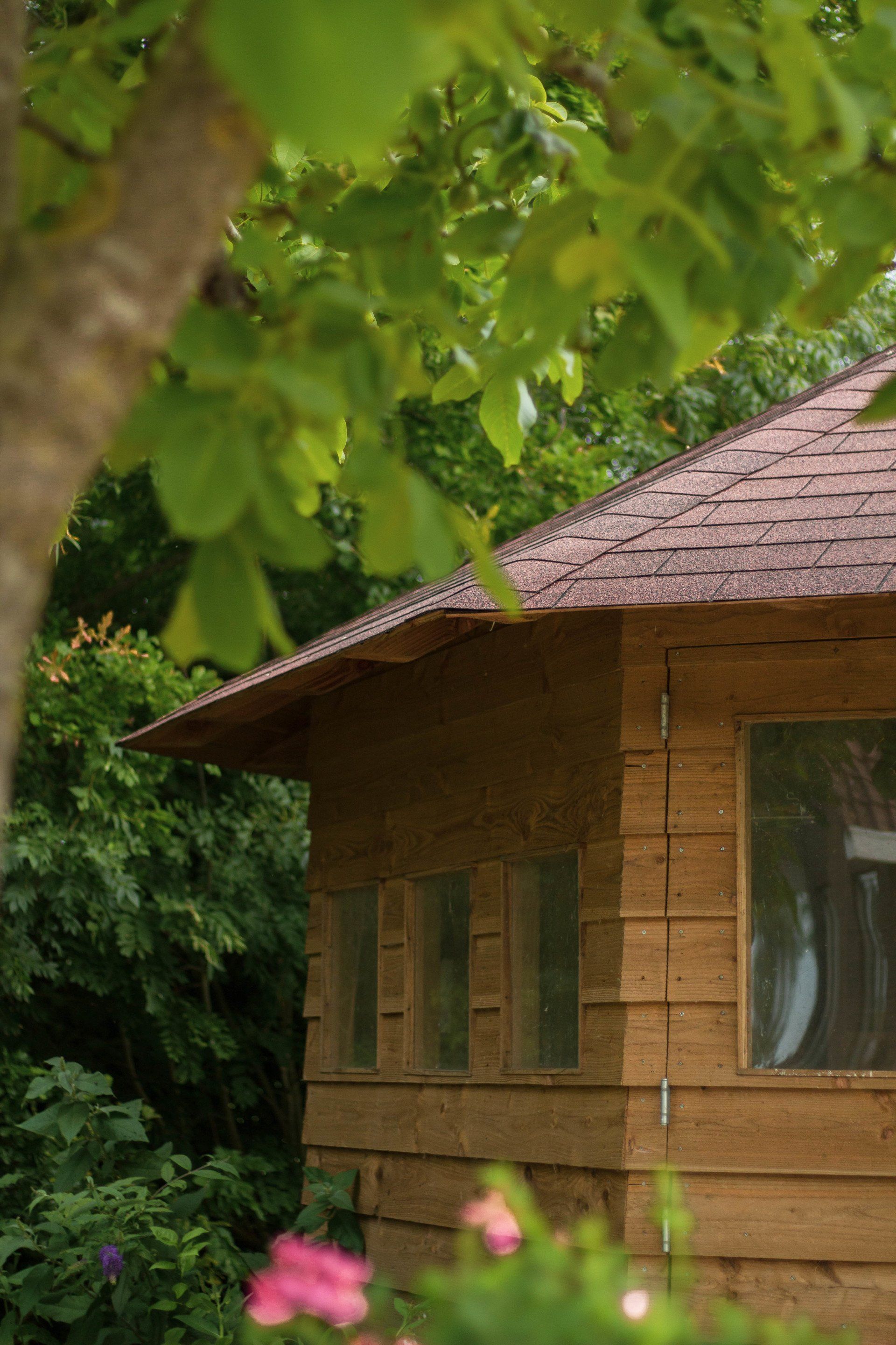 Houten hut met bruin dak, ramen en groene begroeiing.