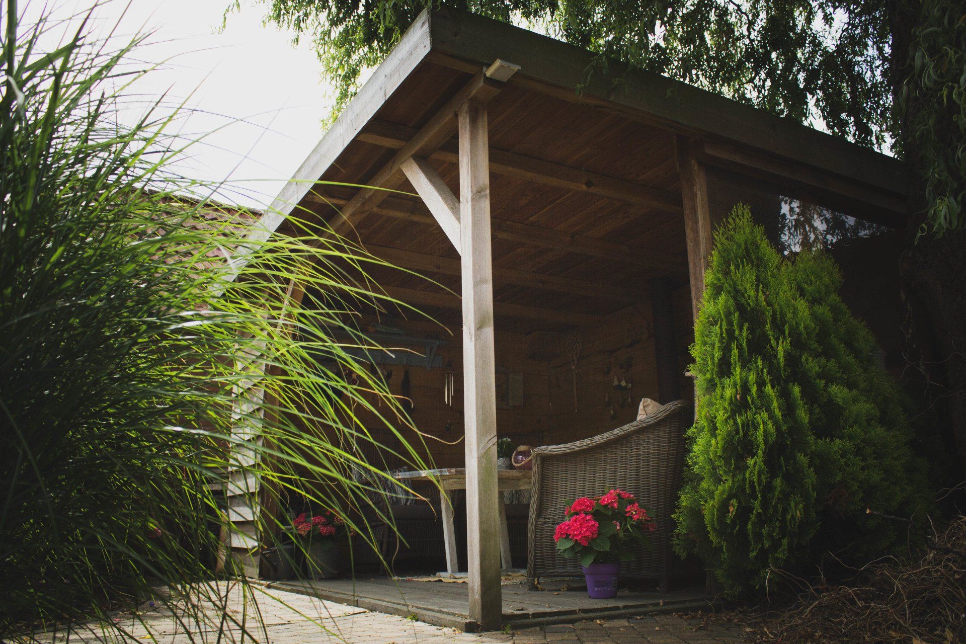 Houten tuinhuisje met zitgelegenheid en planten.