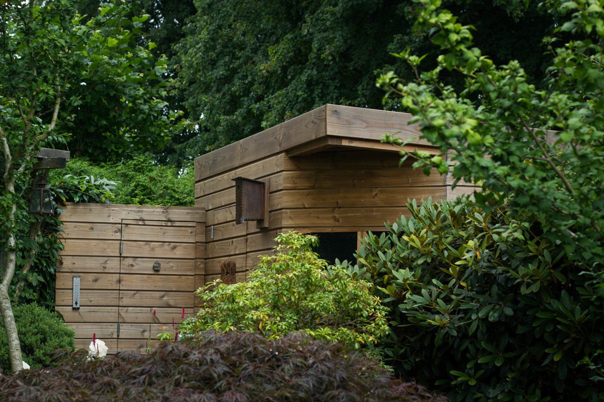 Houten constructie met betonnen dak, verscholen tussen weelderig groen.