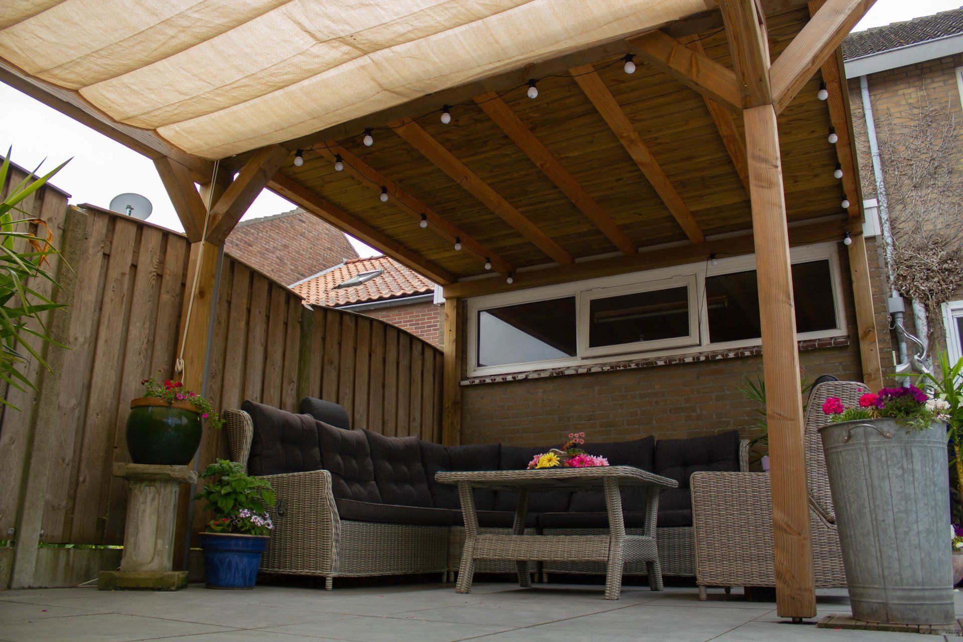 Terras met een houten pergola, zitgelegenheid en sierplanten.