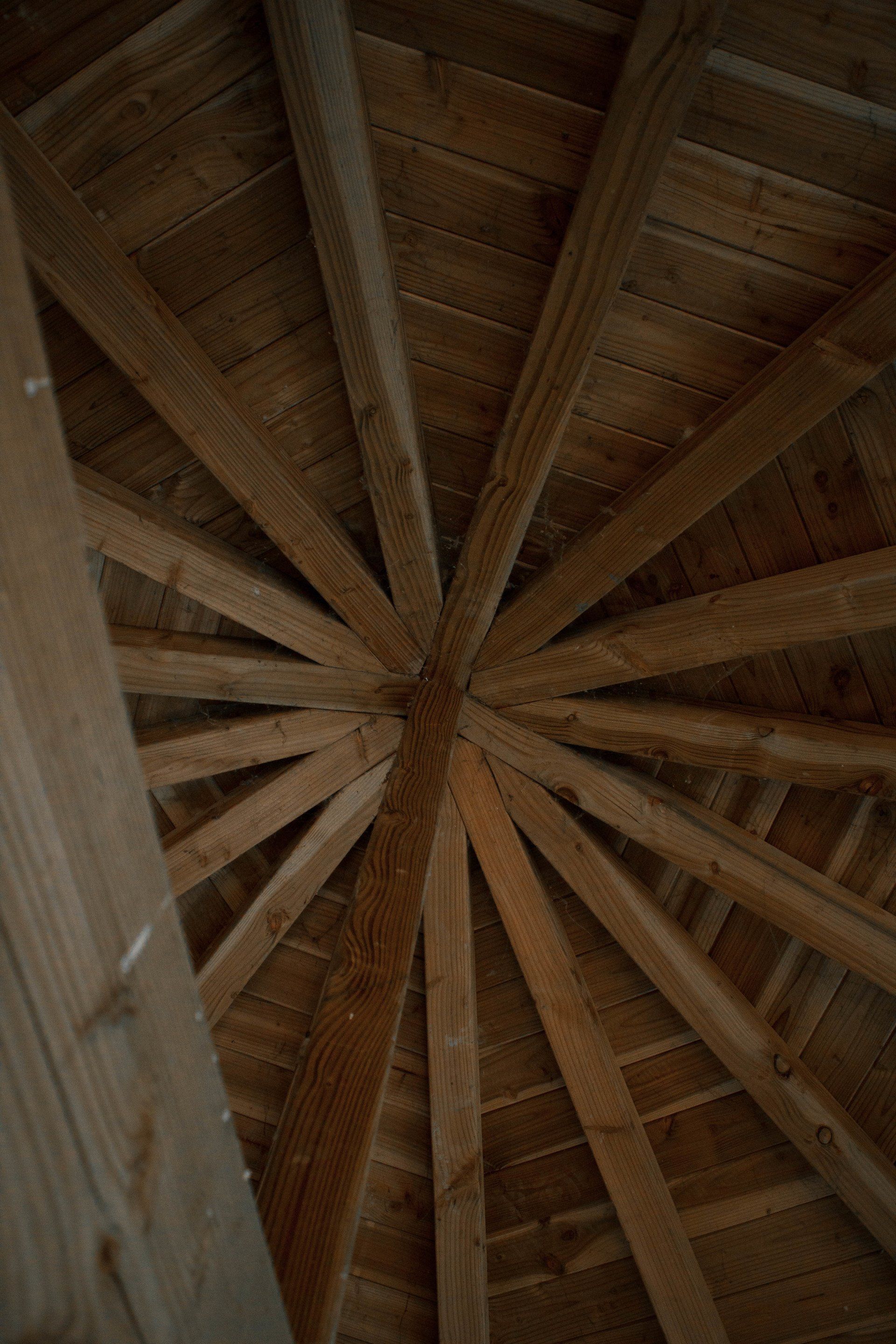 Houten balken stralen vanuit een centraal punt uit en vormen een cirkelvormige plafondconstructie.