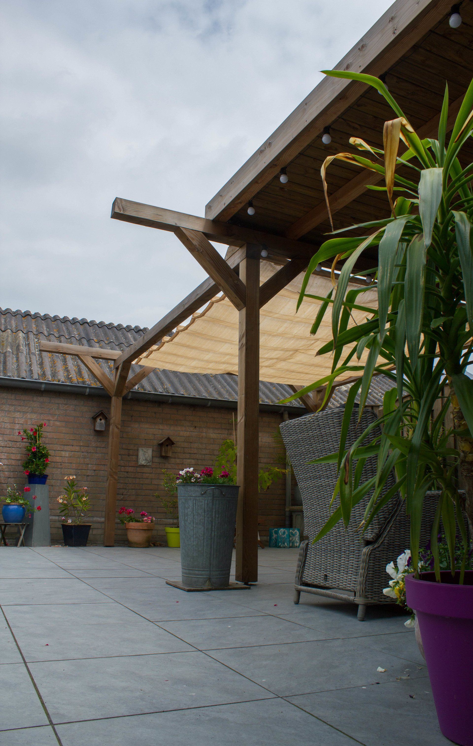 Terras met houten pergola, bakstenen muur op de achtergrond, planten in potten.