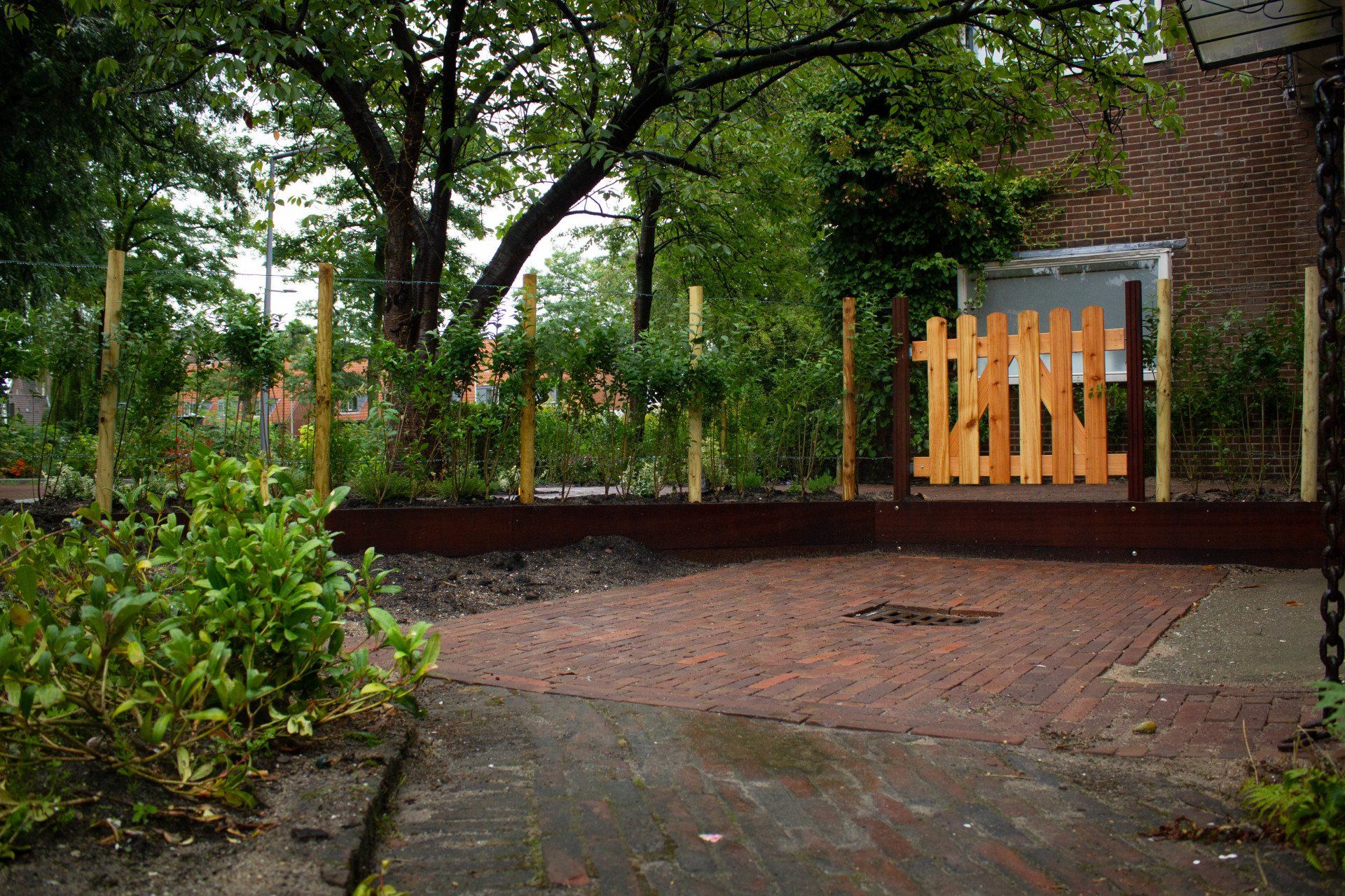 Een tuinpad leidt naar een klein houten hek, omgeven door een verhoogd bloembed en planten.