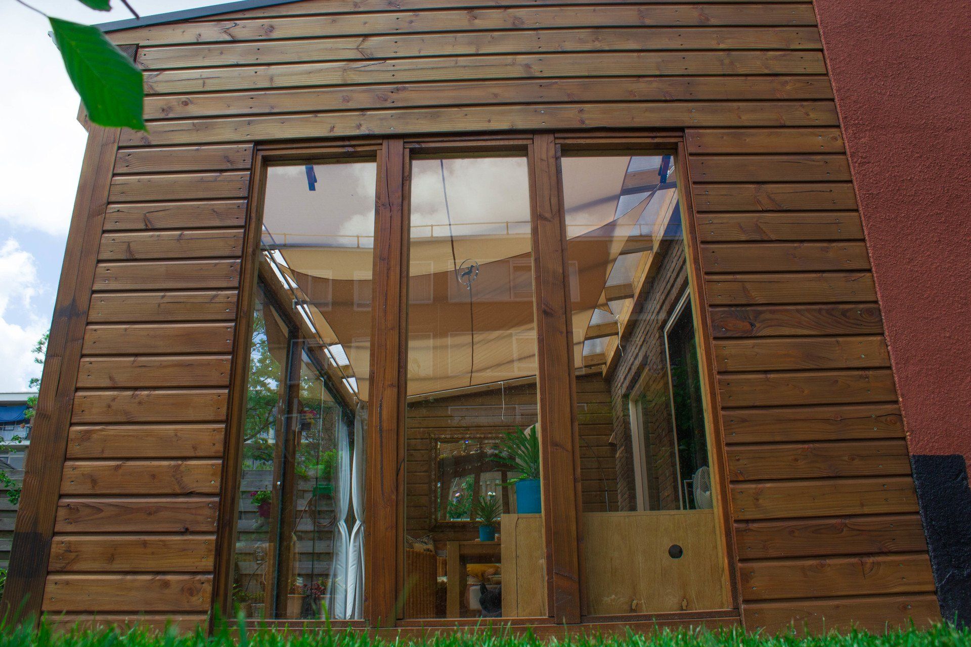 Houten gebouw met grote glazen deuren. Groen gras ervoor, de lucht zichtbaar door de ramen.