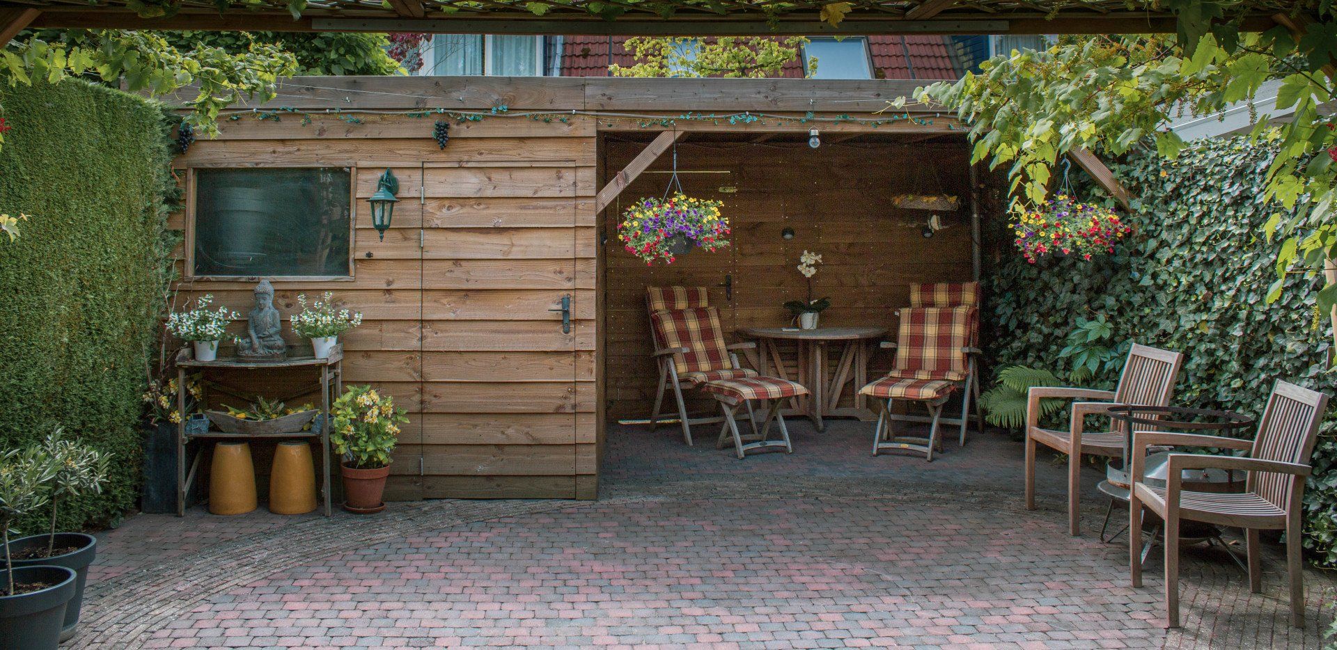 Een houten terras met zitgelegenheid, planten en een beschutte plek.