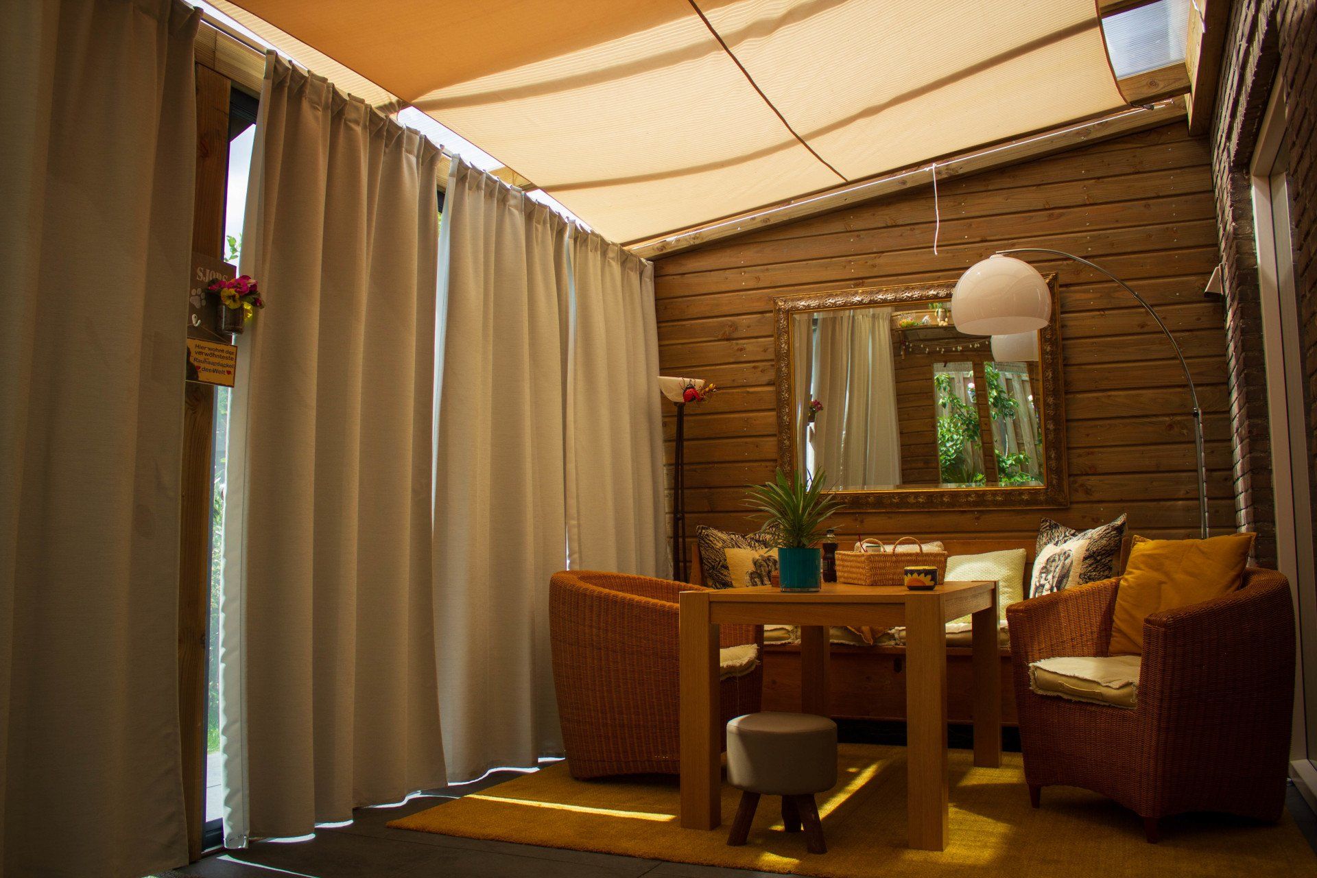 Zonnige, afgesloten patio met houten wanden, rieten meubels en transparante gordijnen.
