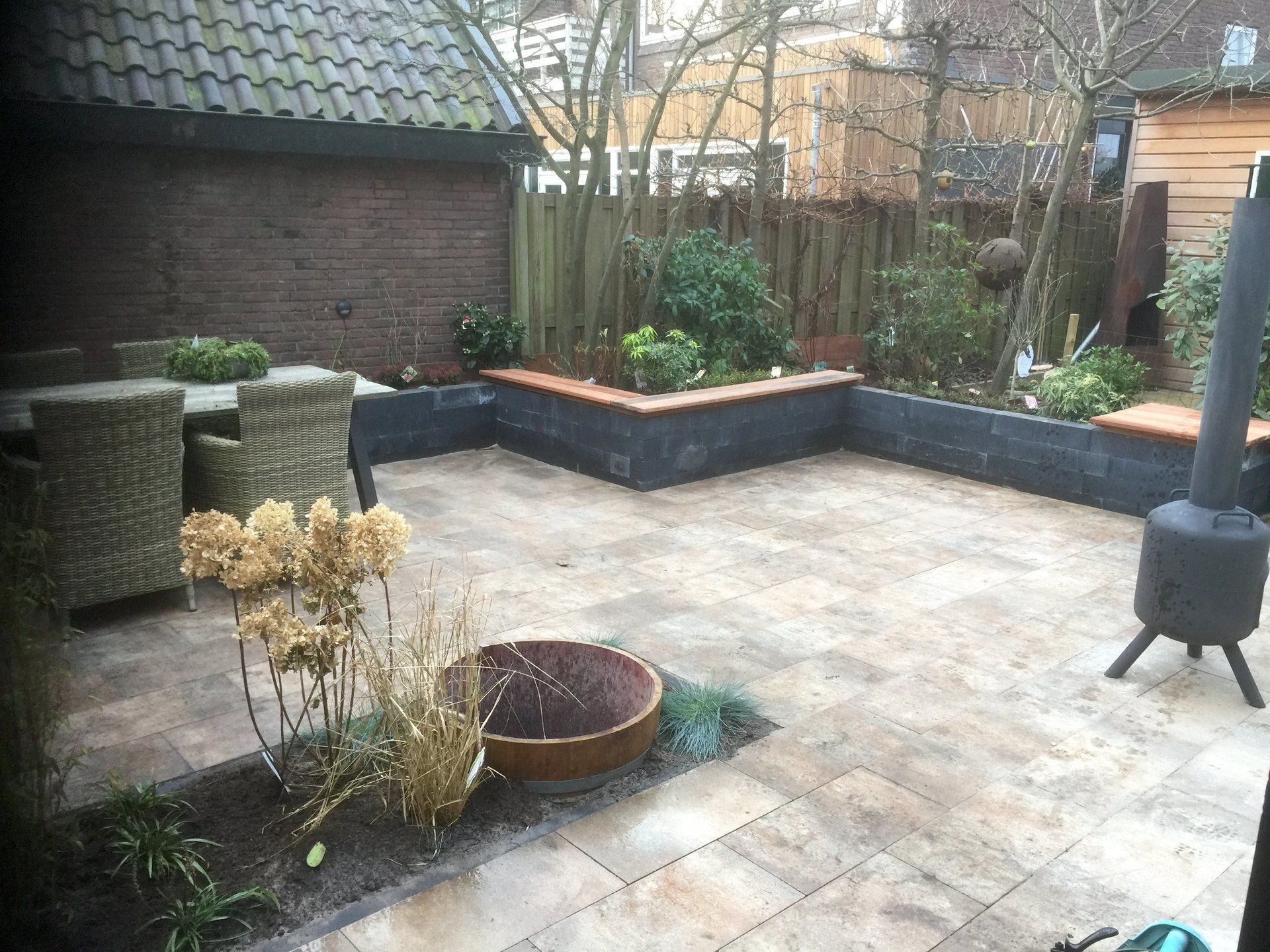 Terras met stenen bestrating, verhoogde plantenbakken en tuinmeubilair.