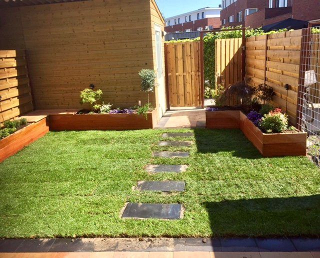 Kleine achtertuin met houten plantenbakken, een stenen pad en groen gras.
