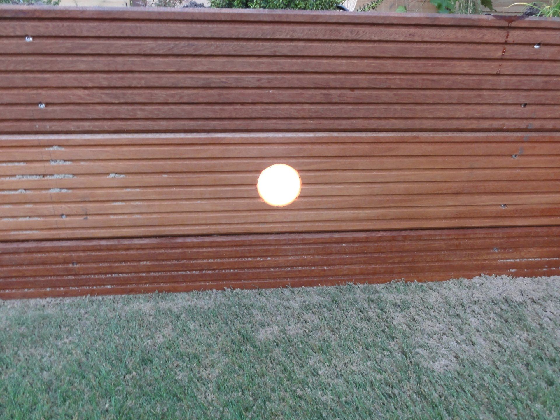 Houten schutting met een gloeiend rond licht, geplaatst tegen een groen gazon.