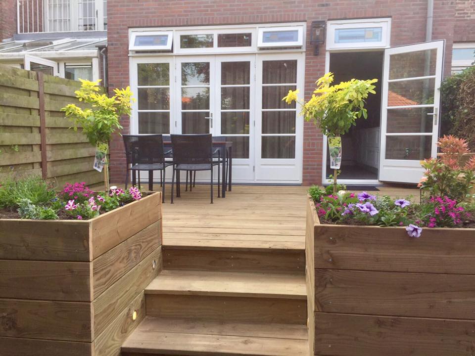 Houten terras met trap, bloembakken met bloemen, dat leidt naar witte openslaande deuren.