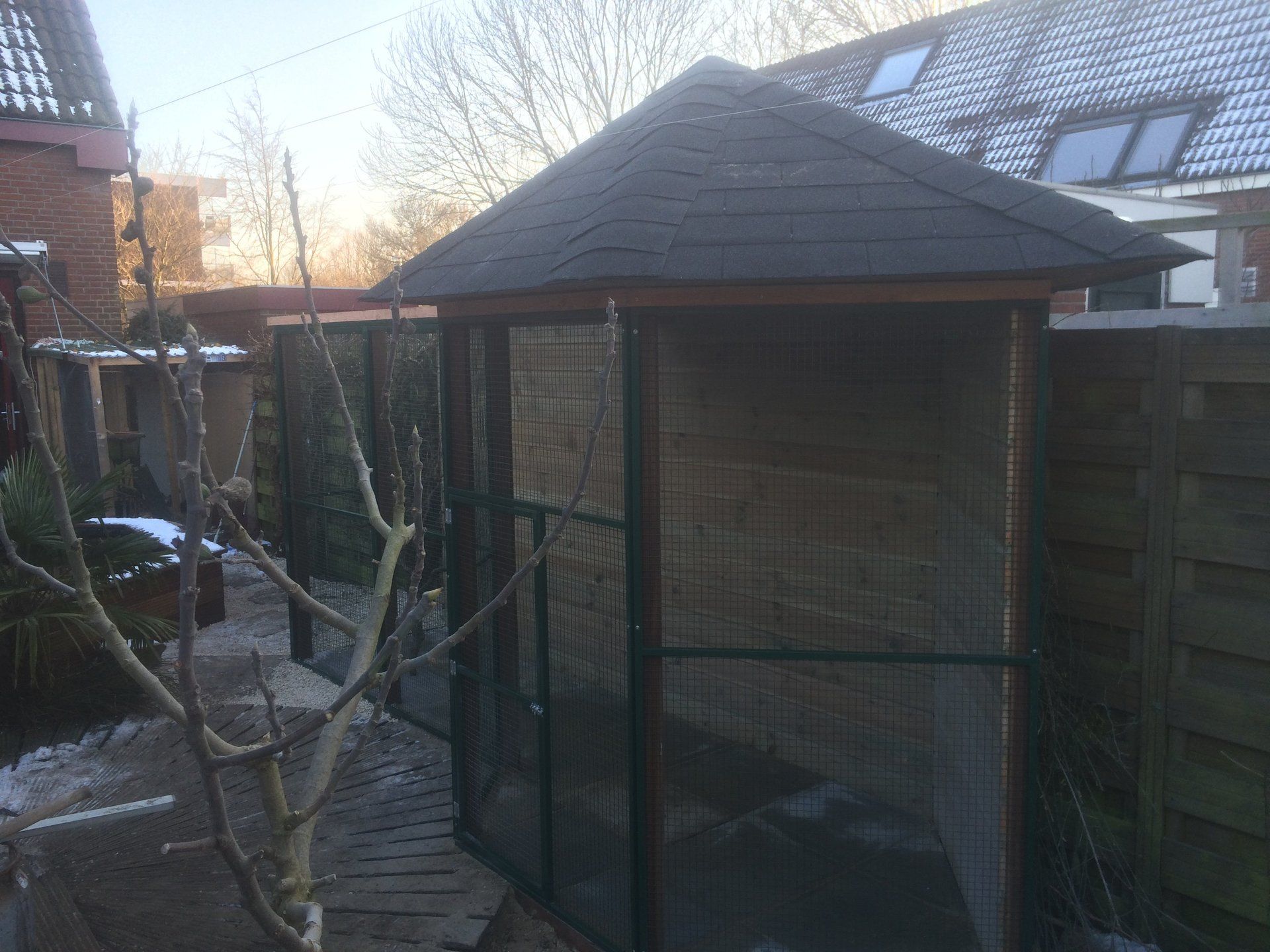 Buitenvolière met een donker dak en wanden van gaas.