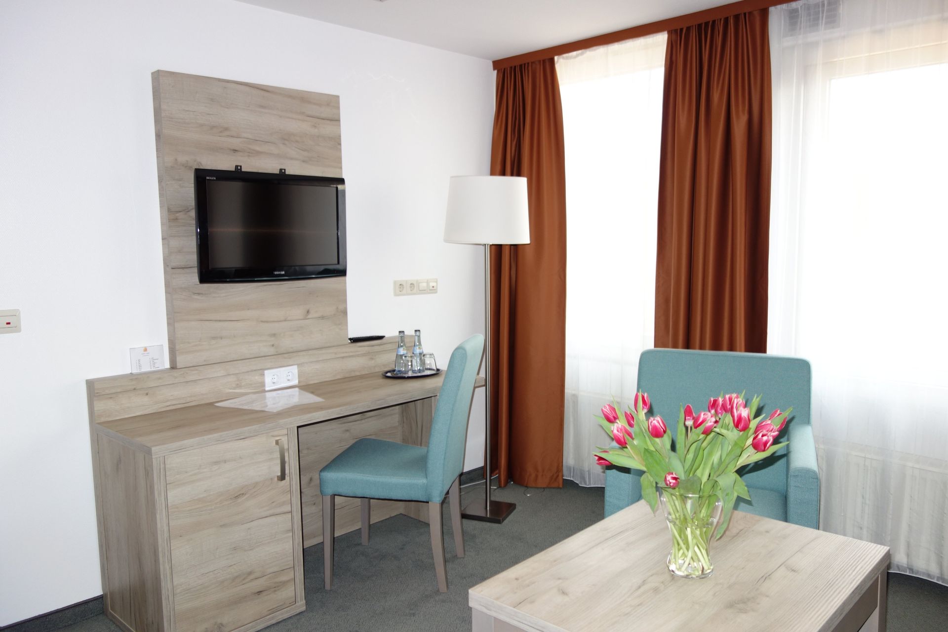 A hotel room with a desk , chair , table and television.
