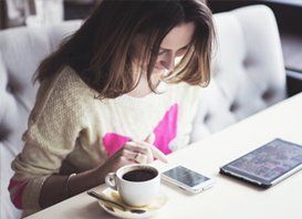 A woman is sitting at a table with a cup of coffee and a cell phone.