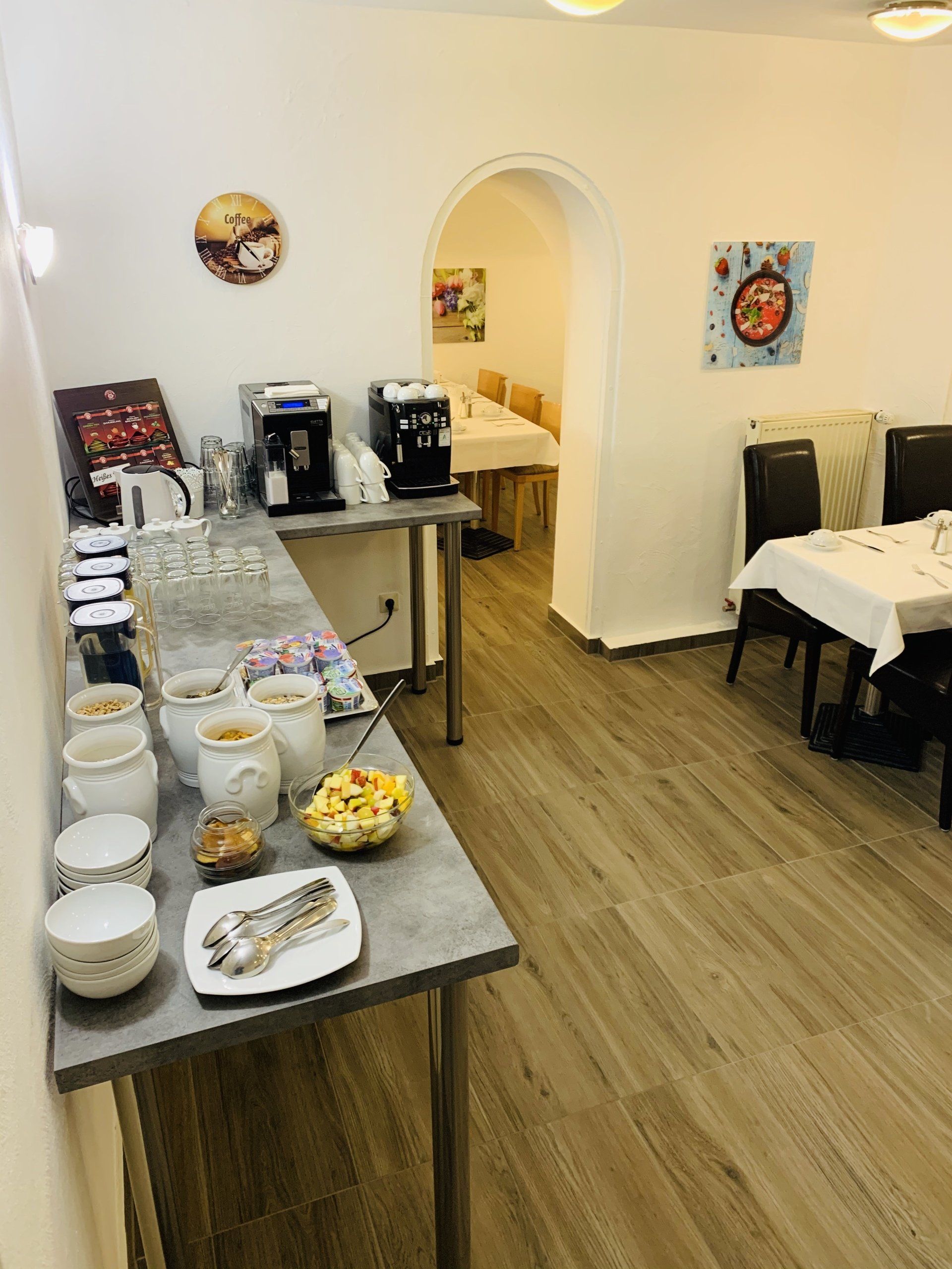 A dining room with tables and chairs and a table with food on it.