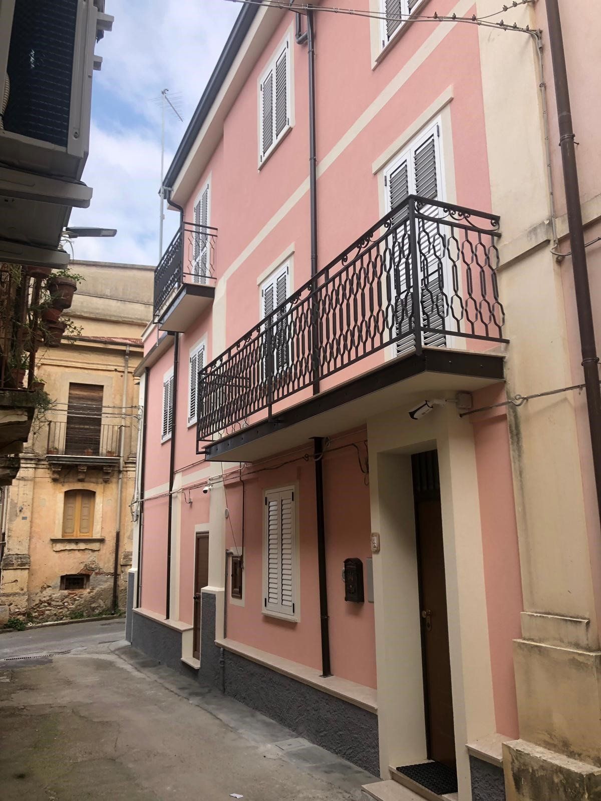 Un edificio rosa con un balcone e una cassetta postale