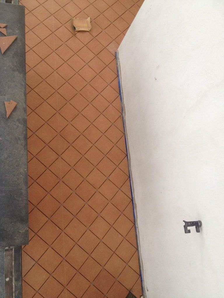 Un pavimento in piastrelle marroni con un muro bianco dietro