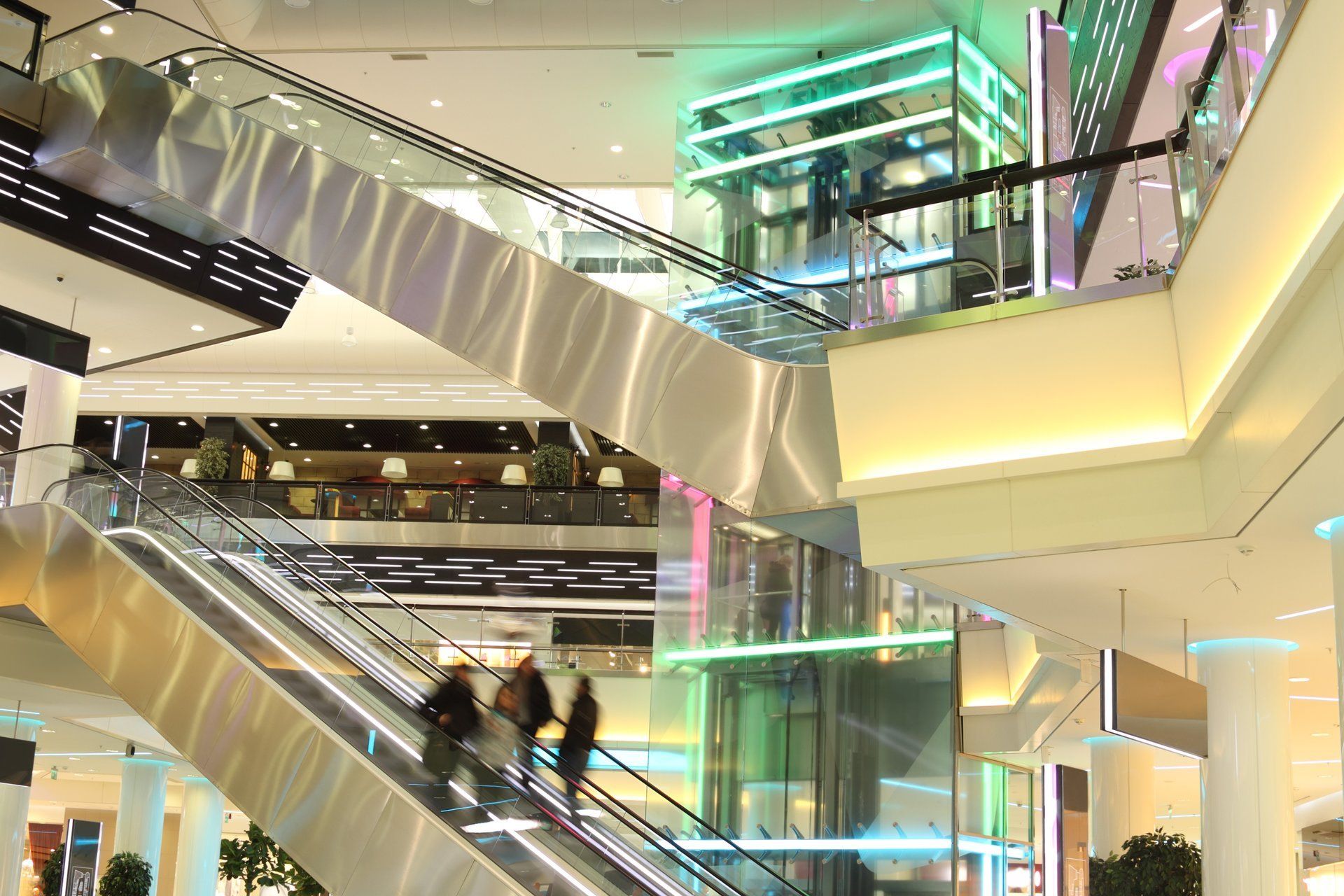 Rolltreppen in einem modernen Einkaufszentrum, auf denen Menschen nach oben fahren.