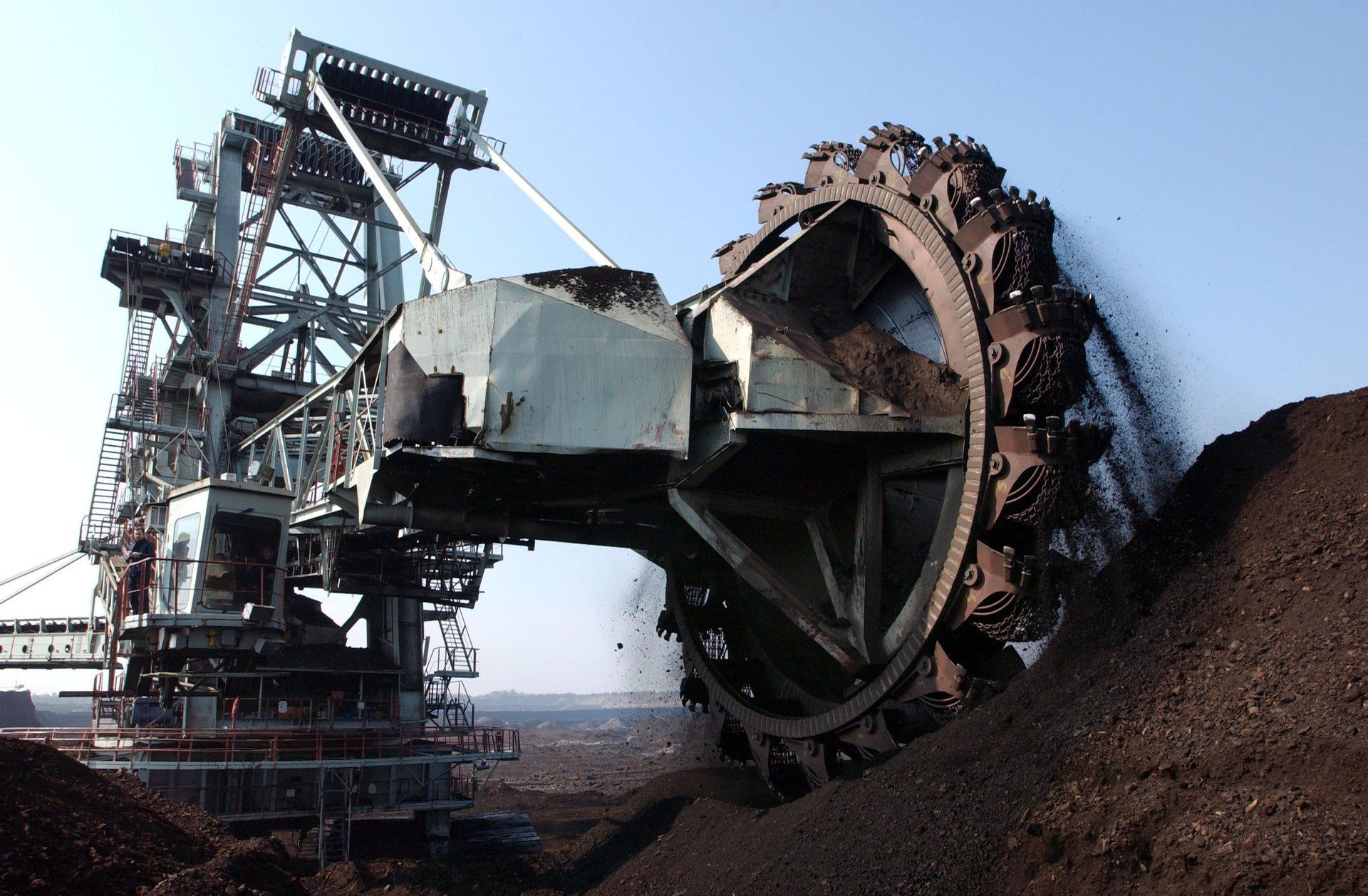 Ein großer, industrieller Radbagger gräbt sich in einen Hügel aus dunkler Erde.