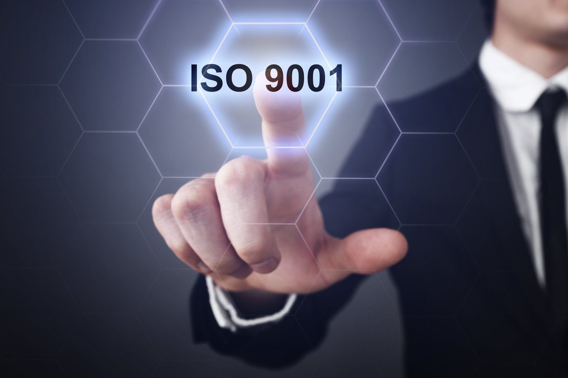 Geschäftsmann zeigt auf ein beleuchtetes Sechseck mit der Aufschrift „ISO 9001“ vor dunklem Hintergrund.