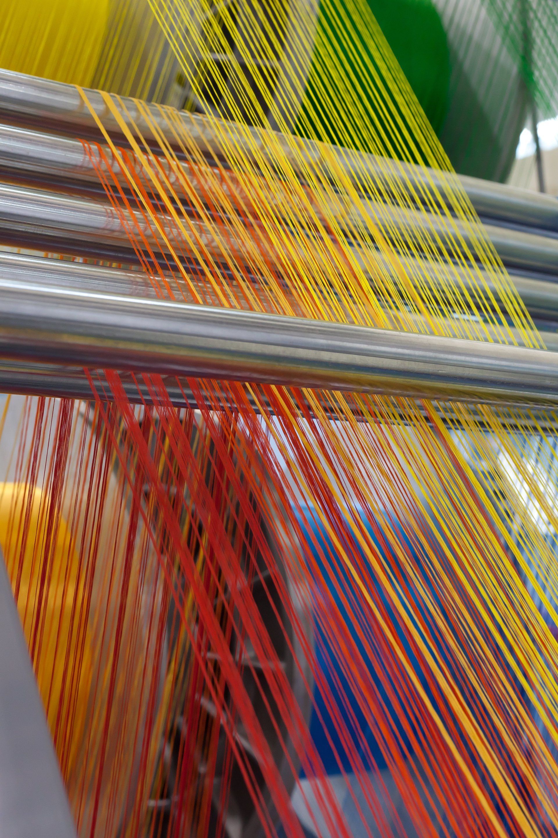 Bunte Fäden auf einer Maschine, die von Rot nach Gelb übergehen, werden in der Textilproduktion verwendet.