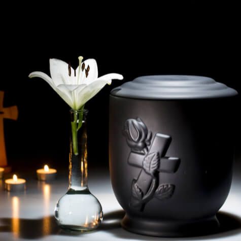 Giglio bianco in un vaso di vetro accanto a un'urna commemorativa nera con candele accese su una superficie scura