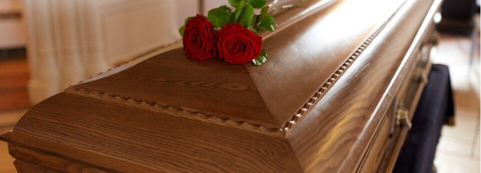 Bara marrone con rose rosse sopra, in un contesto funebre.