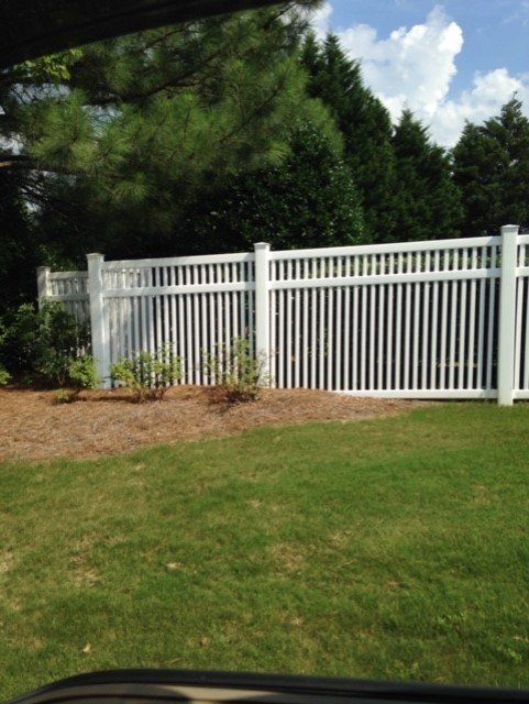 White picket fence in a green yard with a blue sky and trees in the background.